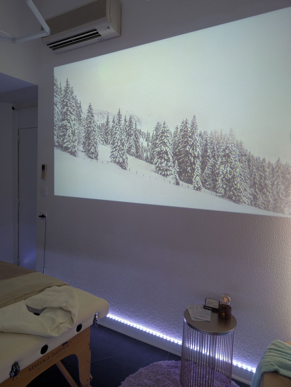 Escale à la montagne : la salle de massage, avec une forêt de sapins enneigés projetée sur le mur